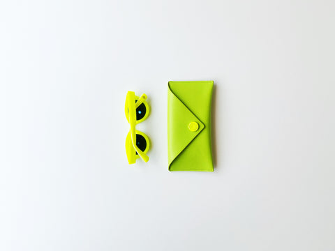 a pair of neon yellow sunglasses laying next to a square yellow case | eyedeals optometry